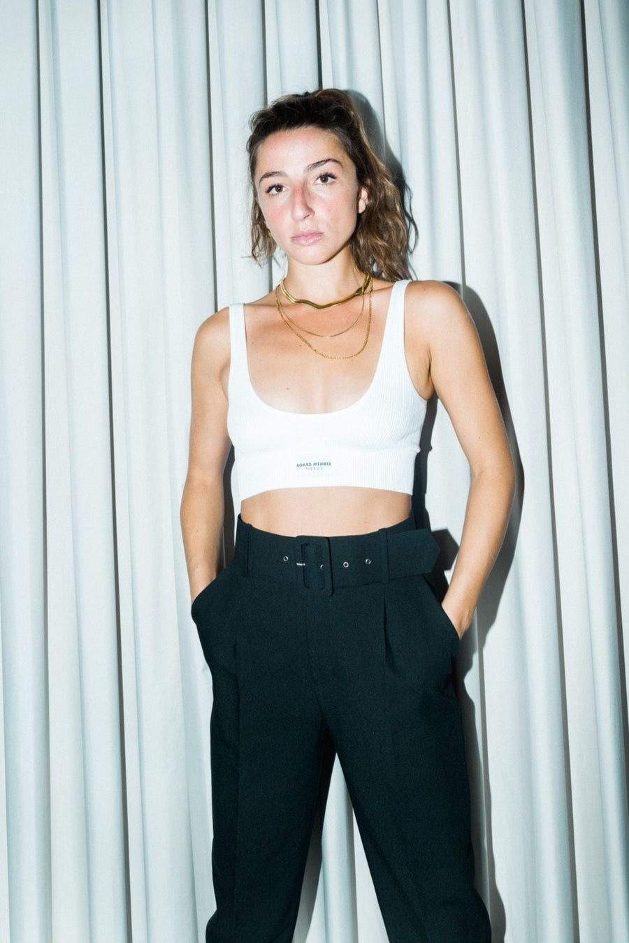 Model wearing THE B.O.D white seamless ribbed bralette and black suit pants, standing in front of a light grey curtain. The Board of Directors Ribbed Bra in White aka Flat White 